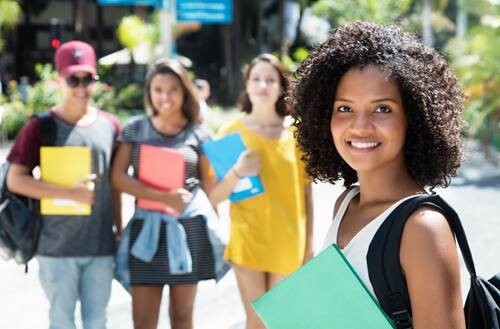 A student holding a green binder with three other students standing off in the background.