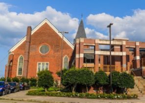 The front of a big brick building with tree lined up around the front corner.