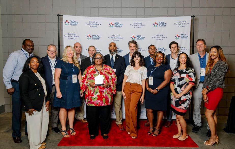 Big group of individuals posing with an award while standing in front of a North Carolina Housing backdrop.