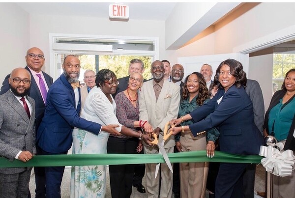 A group of individuals getting ready to cut a green ribbon. 