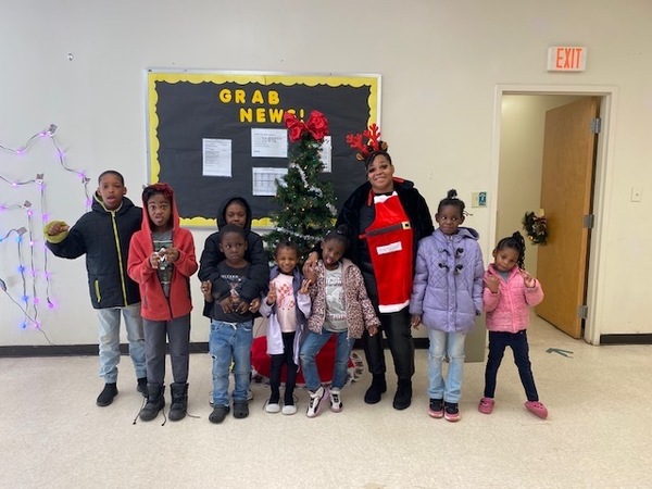 A woman standing next to a group of children in front of a Christmas tree.