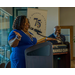 A woman in a blue dress gesturing with her hands as she speaks at the podium.